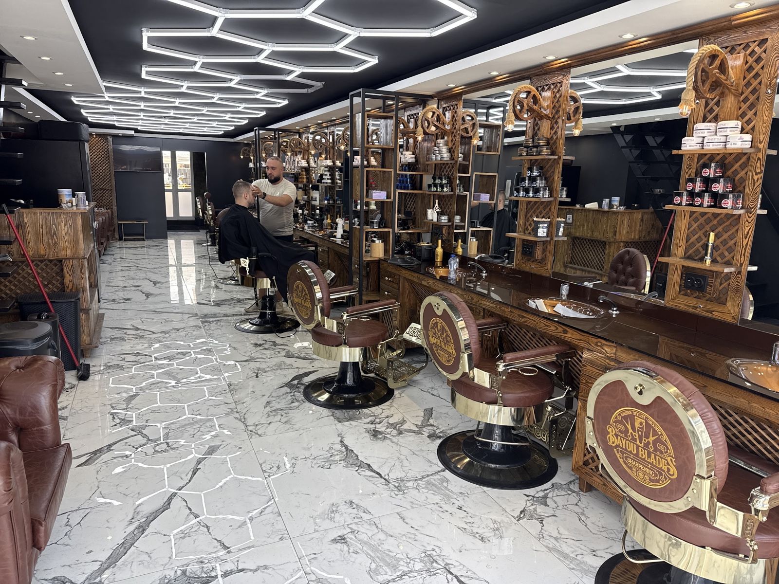 Interieur van RM Barbershop: rij leren barberstoelen, marmeren vloer en zeshoekige ledverlichting