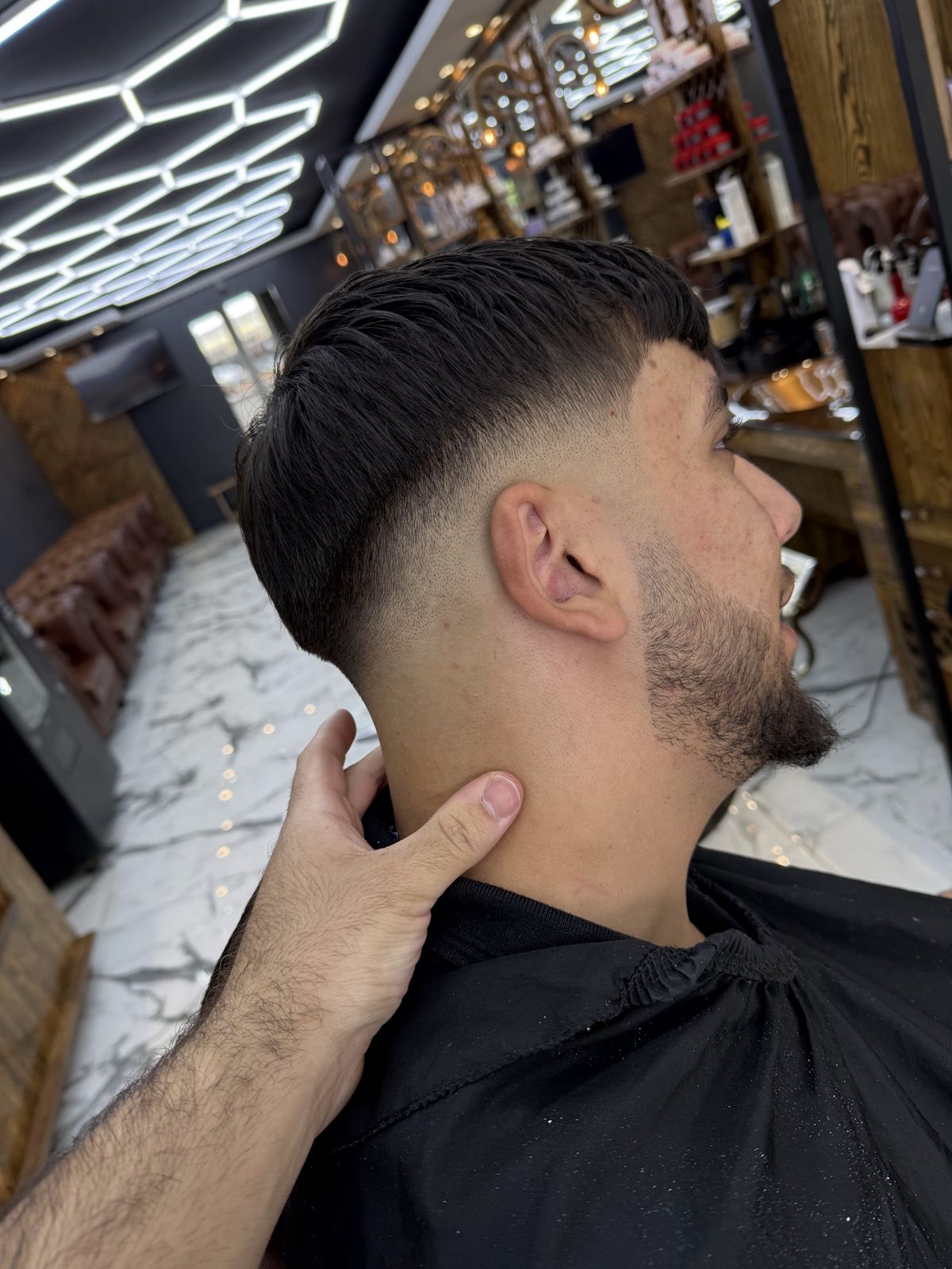 Low taper fade met getextureerde pony onder de zeshoekige ledverlichting
